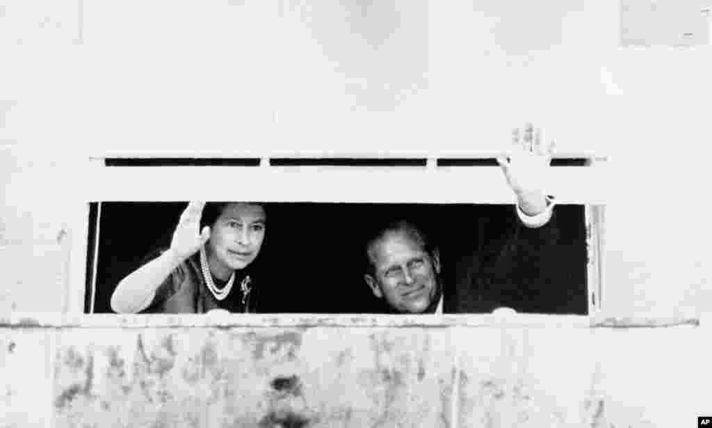 Britain's Queen Elizabeth II and her husband, Prince Philip, wave to a crowd of well-wishers, Aug. 10, 1977, from a partly closed window in Hillsborough Castle, 12 miles south of Belfast, Northern Ireland. Violence is marking the Queen's silver jubilee visit to the troubled province.