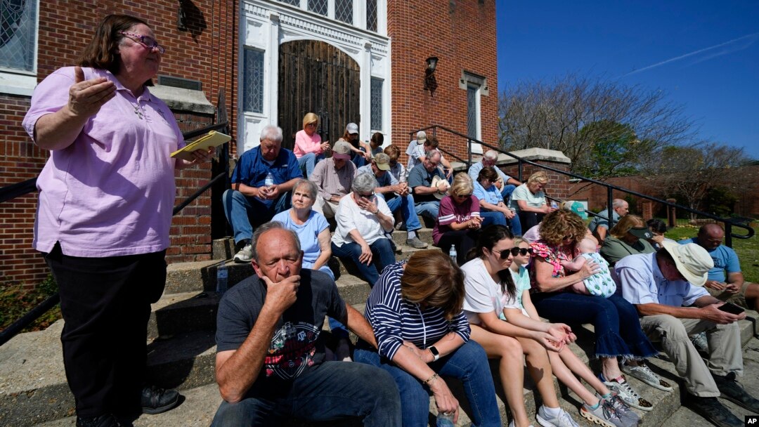 Rev. Mary Stewart, left, of Rolling Fork United Methodist Church, leads a prayer as people affected by Friday's tornado worship on the steps of the church, in Rolling Fork, Mississippi, March 26, 2023.