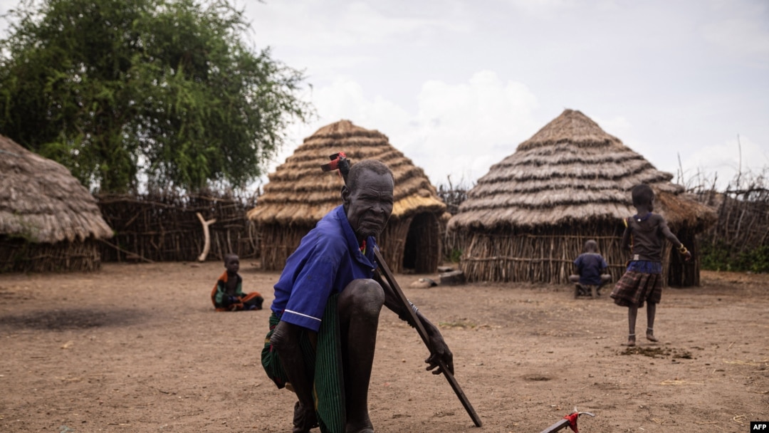 Mzee mmoja akiwa na watoto wake wamekaa nyumbani kwao huko Karamoja, Uganda, tarehe 24 Mei 2022. Picha na Badru KATUMBA/AFP.
