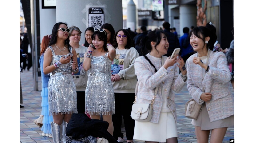 La gente espera en fila cerca de un cartel para tomarse fotografías, mientras otros, a la derecha, reaccionan a su selfie antes del concierto de Taylor Swift en el Tokio Dome en Tokio, el sábado 10 de febrero de 2024. (Foto AP/Hiro Komae)
