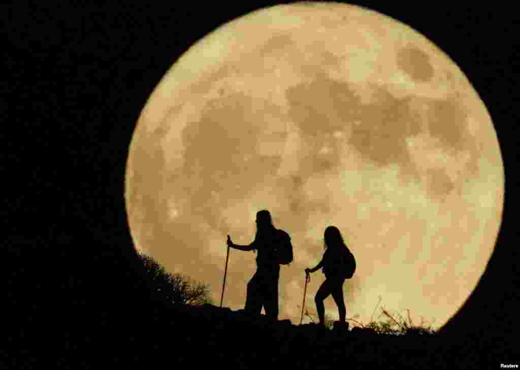 Women walk up a mountain with the full moon known as the "Sturgeon Moon" looms in the background, in Arguineguin, on the island of Gran Canaria, Spain, Aug. 1, 2023.
