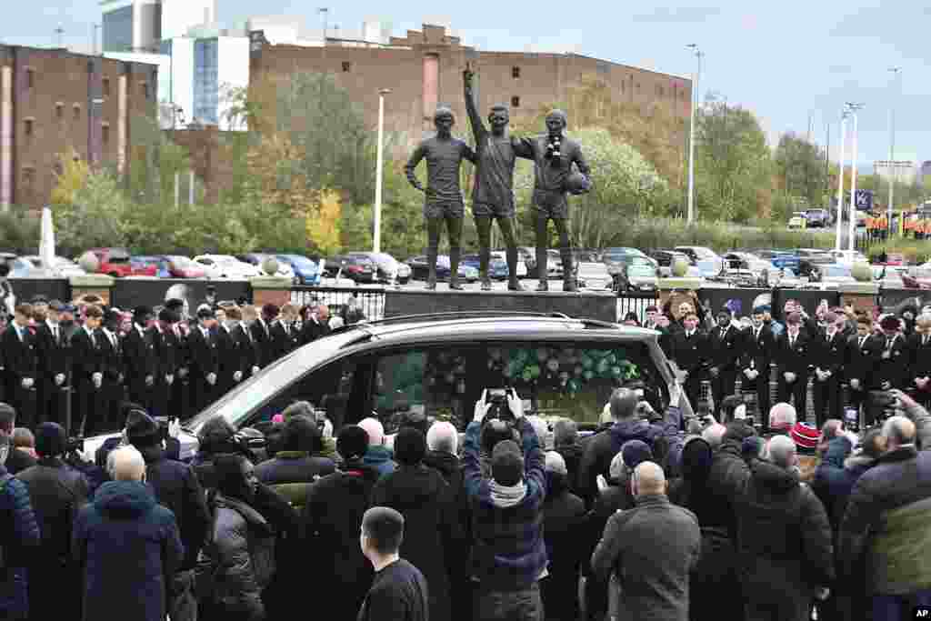 The cortege of English soccer icon Bobby Charlton passes by the statue of Manchester United trio of George Best, left, Denis Law, center, and Sir Bobby Charlton outside Old Trafford stadium on its way to the funeral service at Manchester Cathedral in Manchester, England.