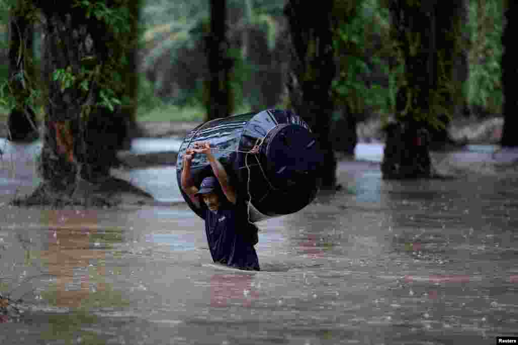 A man carries an empty water tank through a flooded area after the impact of the tropical storm Julia, in Progreso, Hondura, Oct. 9, 2022.