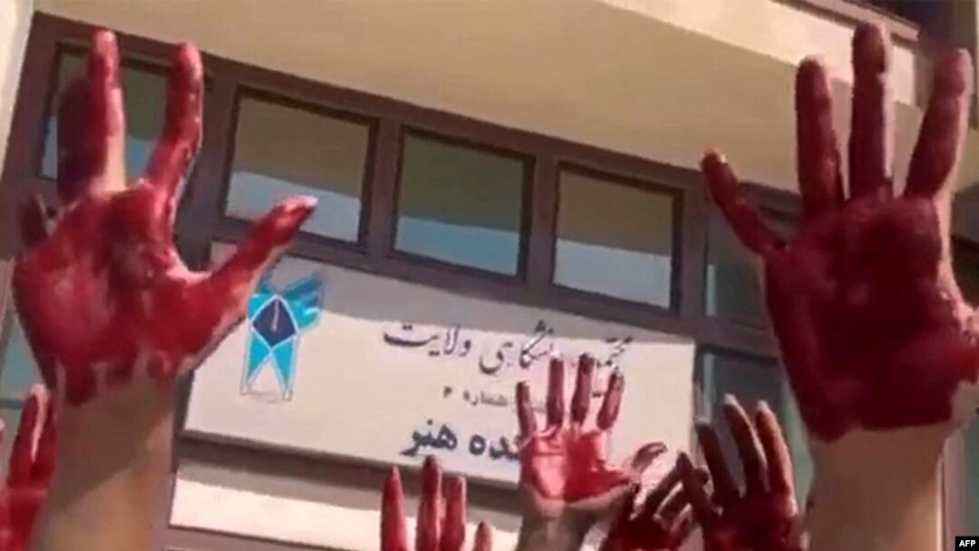 This image grab from a UGC video made available on Twitter on Oct. 9, 2022, shows Iranian students from the Faculty of Arts at Tehran's Azad University participating in a protest with their palms covered in red paint to symbolize blood. (Photo by UGC/AFP)