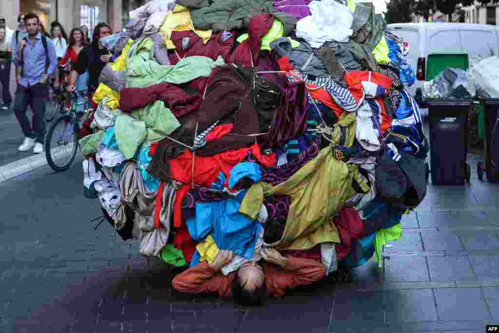 Actor and director Dorian Chavez (C) pushes a ball covered by clothes as part of a performance called "Sisypholia" denouncing the "absurdity" of overconsumption in Toulouse, southwestern France, Oct. 5, 2022, during the "Biennale des arts vivants de Toulouse."