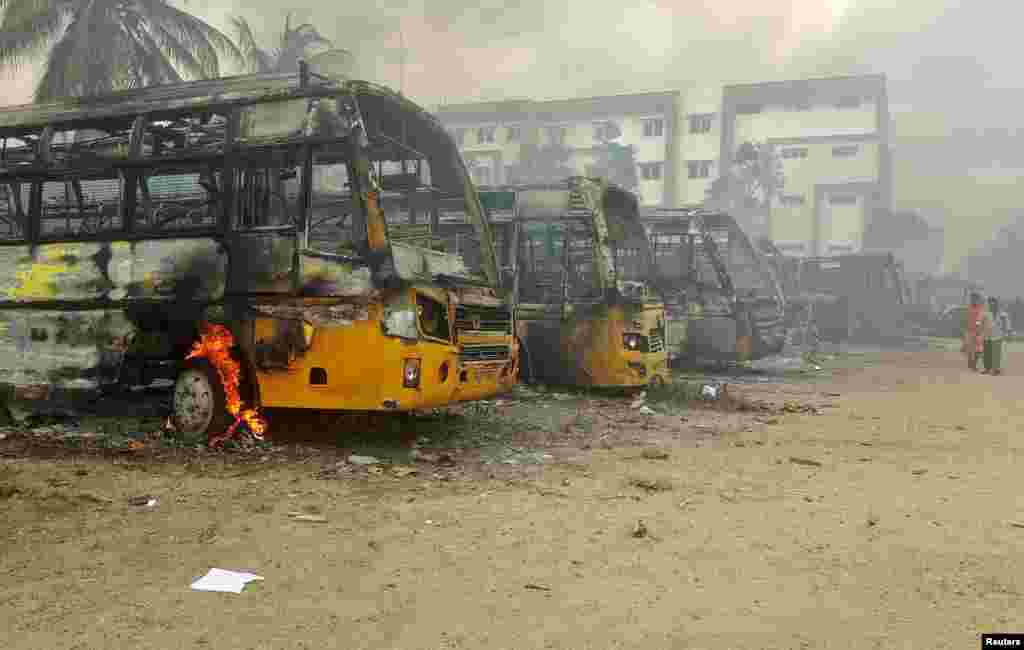 People walk past damaged school buses that were set on fire by a mob in the school campus after a female student's death in Kallakurichi district in the southern state of Tamil Nadu, India.