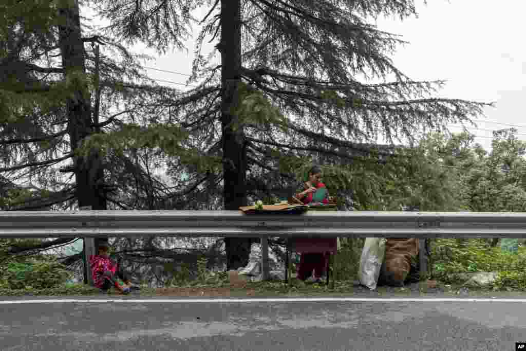 A child looks at a phone as his mother roasts corn on the cob to sell by the roadside in Dharmsala, India.