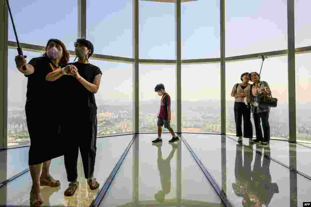 Visitors pose for selfies as a young boy walks on the observation deck at the Lotte World Tower Seoul Sky in Seoul, South Korea.
