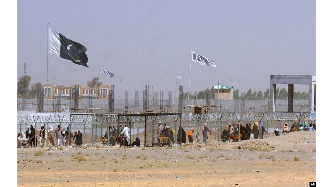 FILE - Pakistan and Taliban flags flutter on their respective sides while people walk through a security barrier to cross border at a key border crossing point between Pakistan and Afghanistan, in Chaman, Pakistan, Aug. 18, 2021.