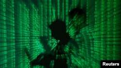 FILE - An illustration picture shows a projection of binary code on a man holding a laptop computer. British police have arrested a 16-year-old boy in London over a cyberattack on telecoms firm Talk Talk.