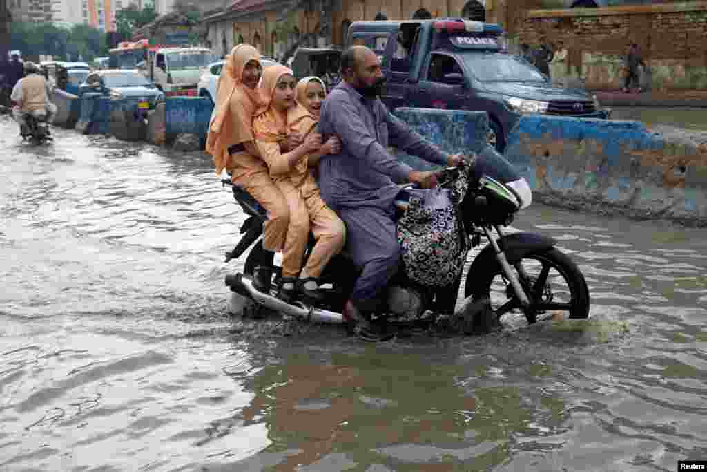 A man and students ride on a motorcycle on a flooded road, following rains during the monsoon season in Karachi, Pakistan.