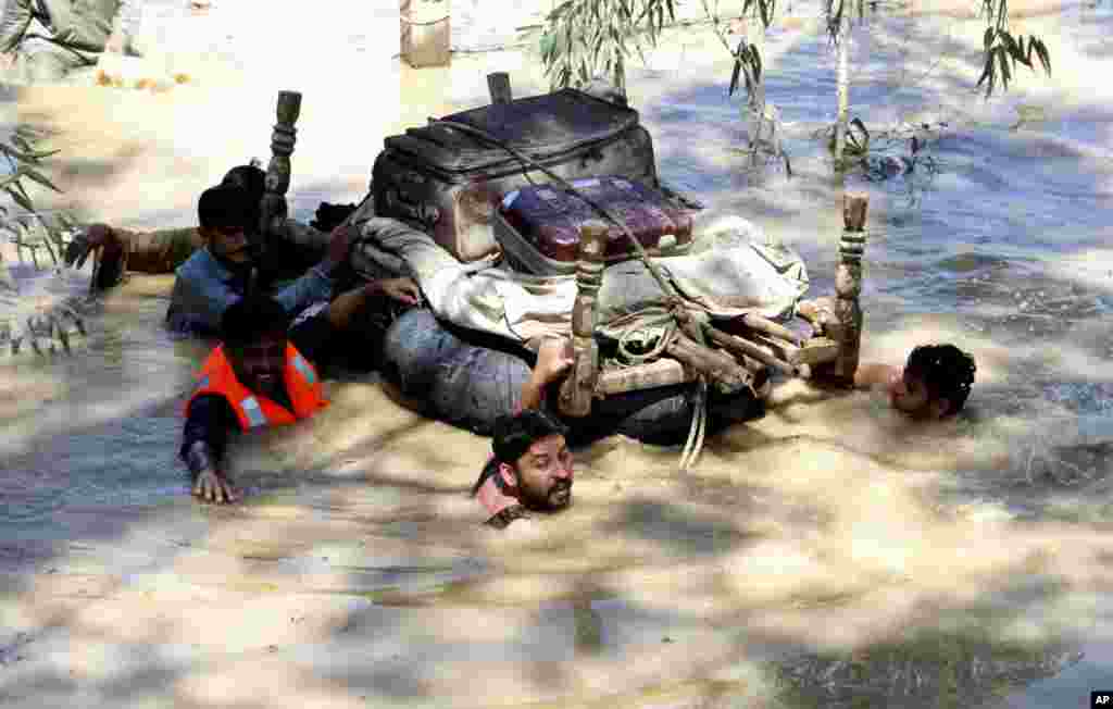 Displaced people float belongings salvaged from flood-hit homes through a flooded area, on the outskirts of Peshawar, Pakistan