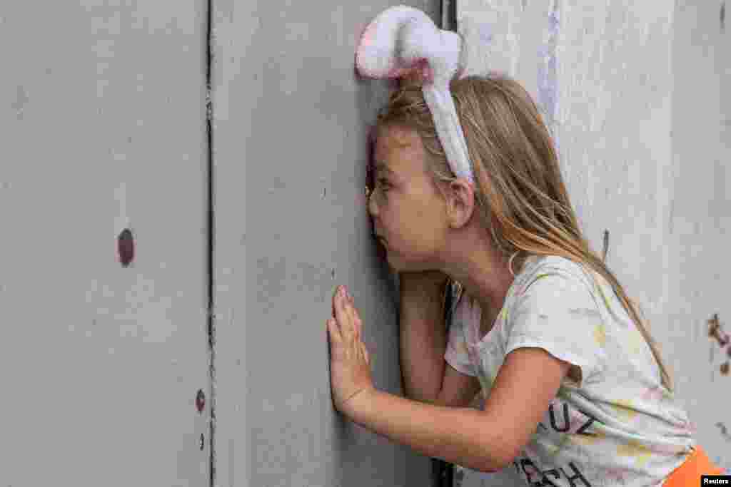 Anhelina looks through a shrapnel hole in a fence after a recent Russian military strike in Mykolaiv as Russia's attack on Ukraine continues, in Mykolaiv.