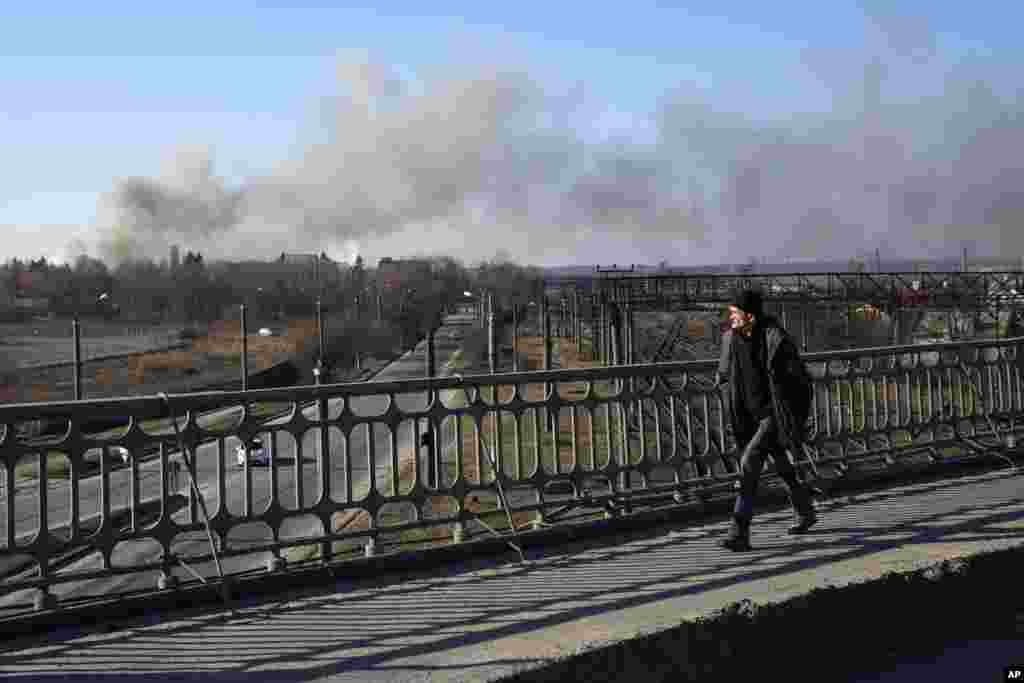 Un peatón mira una nube de humo que se eleva después de una explosión en Lviv, Ucrania occidental, el viernes 18 de marzo de 2022. El alcalde de Lviv dice que misiles impactaron cerca del aeropuerto de la ciudad el viernes temprano. 