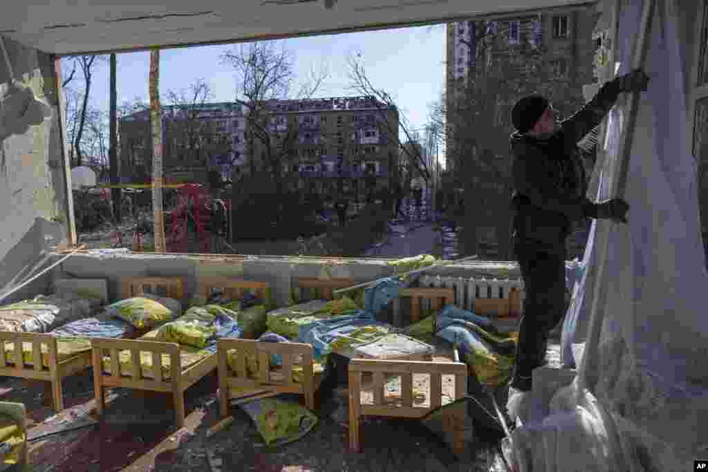 Un hombre quita una cortina destruida dentro de una escuela dañada junto a otros edificios residenciales, en Kiev, Ucrania, el viernes 18 de marzo de 2022. Las fuerzas rusas intensificaron su ataque contra las ciudades ucranianas el viernes, con nuevos ataques con misiles y bombardeos en los bordes de la capital, Kiev, y la ciudad occidental de Lviv, mientras los líderes mundiales presionaban para que se investigaran los repetidos ataques del Kremlin contra objetivos civiles, incluidas escuelas, hospitales y zonas residenciales. 