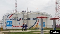 FILE - Workers walk past a storage tank at the Kaleikino oil pumping station of Transneft Kama Region near Almetyevsk, Russia, April 27, 2022.