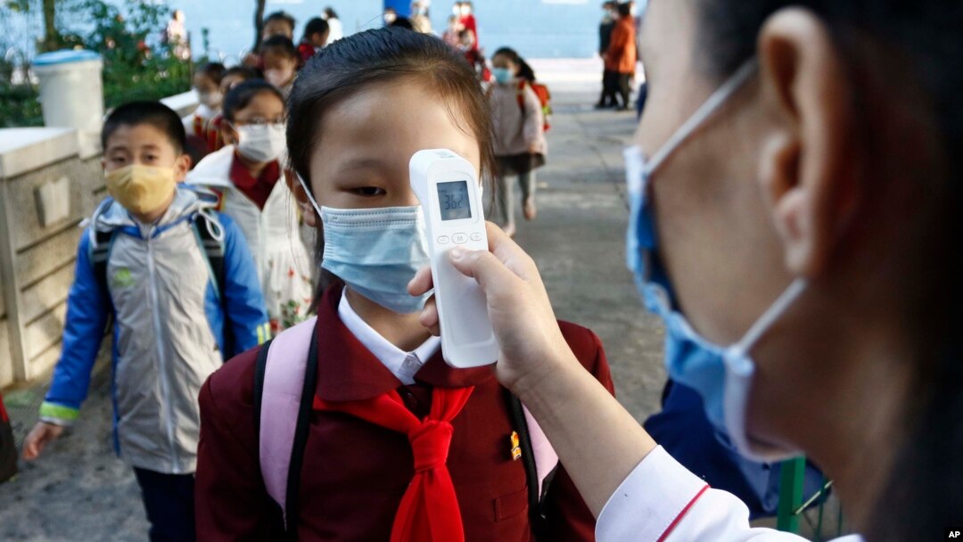 FILE - A teacher takes the body temperature of a schoolgirl to help curb the spread of the coronavirus before entering Kim Song Ju Primary School in Central District in Pyongyang, North Korea, Oct. 13, 2021.