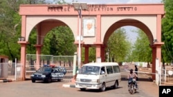 A man rides a motorbike taxi past police vehicles at the entrance of Shehu Shagari College of Education in Sokoto, Nigeria, May 13, 2022. Deborah Yakubu, who was killed May 12 over allegedly blasphemous statements, was a student at the school.