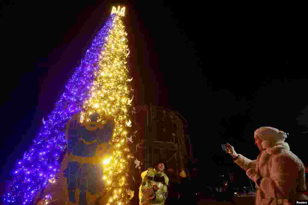 El árbol de Navidad no podía faltar en las celebraciones de fin de año. Con los colores de la bandera de Ucrania, en la Plaza Sofiyska, de Kiev, se alza el árbol frente al que una mujer canta villancicos. 