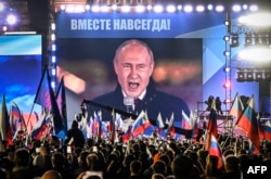 Rais wa Russia Vladimir Putin akihutubia mkutano wa maadhimisho ya majeshi yake kuingia kwa mabavu katika mikoa minne ya Ukraine iliyovamiwa na majeshi ya Russia, huko Moscow Sept. 30, 2022. Maneno juu ya picha yake yanamaanisha "Milele Tukopamoja."