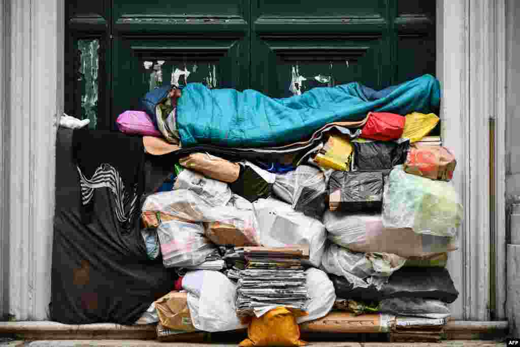 A homeless man sleeps on a pile of plastic bags and newspapers under a porch in Rome, Italy.