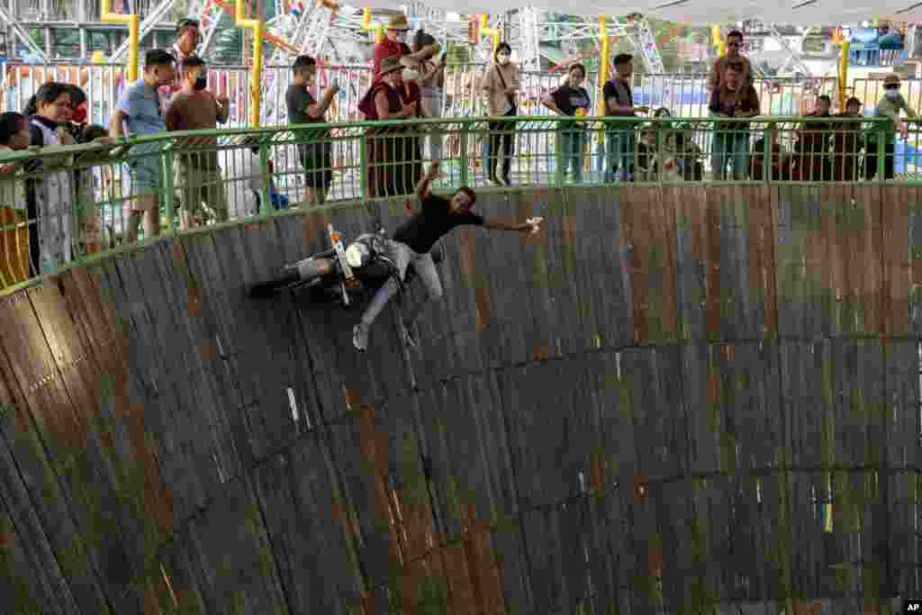 Gulfam Raza sits sideways on his fast moving Royal Enfield motorcycle in an enclosure known as Maut ka Kuan, or the well of death, at a local fair in Dharmsala, India, April 9, 2022.