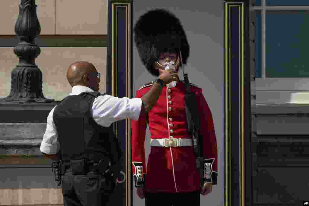 A police officer givers water to a British soldier wearing a traditional bearskin hat, on guard duty outside Buckingham Palace, during hot weather in London, July 18, 2022. The British government have issued their first-ever "red" warning for extreme heat when temperatures may reach 40° C (104° F) for the first time.