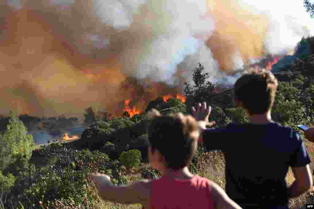 Pedestrians look at a forest fire near Gignac, southern France, July 26, 2022, as the country endures a dry summer with wildfires destroying numerous forests across France.