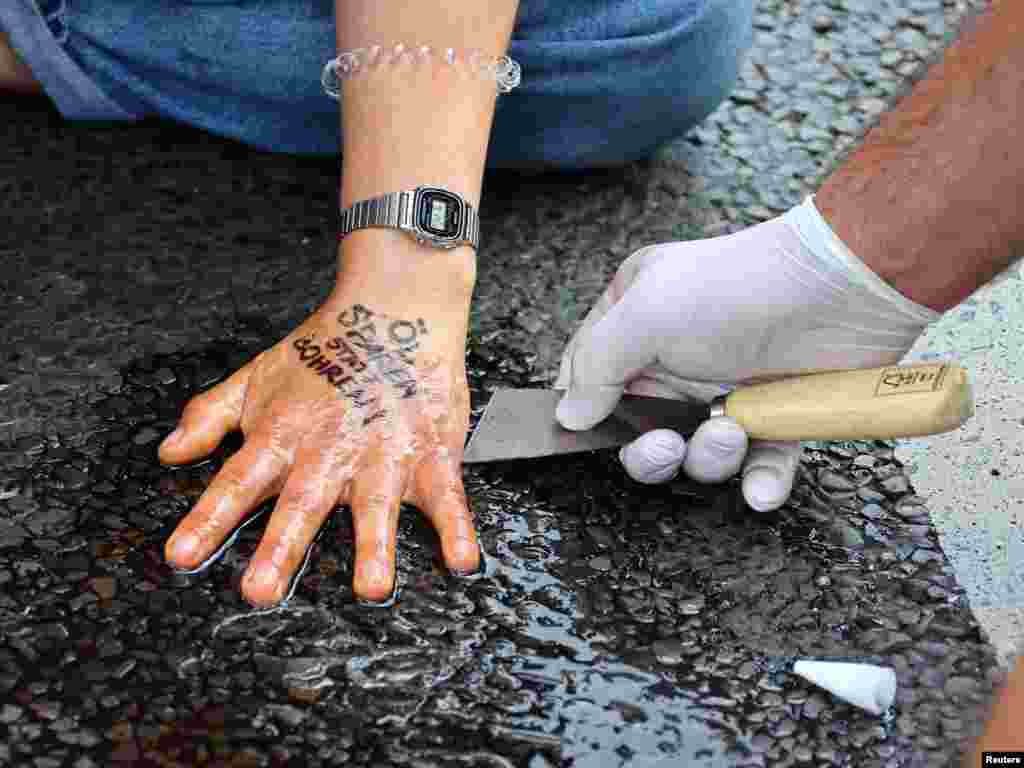 A police officer removes glue from the hand of a Letzte Generation (Last Generation) activist that reads "save oil instead of drill oil," blocking a road under the slogan "Let's stop the fossil madness!" for an end to fossil fuels and against oil drilling in the North Sea, in Berlin, Germany.