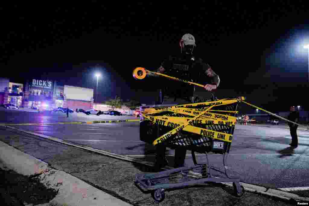 A law enforcement officer attaches a crime scene tape to a shopping cart after a shooting at a mall in the Indianapolis suburb of Greenwood, Indiana, July 17, 2022.