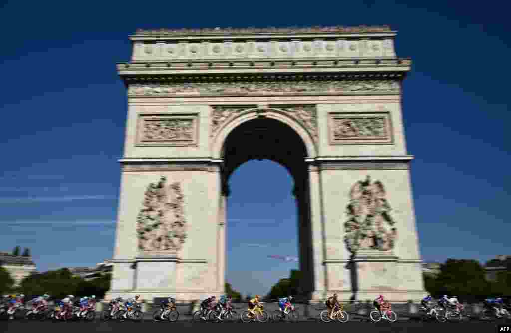 Jumbo-Visma team's Danish rider Jonas Vingegaard wearing the overall leader's yellow jersey (C) cycles with the pack of riders past the Arc de Triomphe during the 21st and final stage of the 109th edition of the Tour de France cycling race, 115,6 km between La Defense Arena in Nanterre, outside Paris, and the Champs-Elysees in Paris, France.