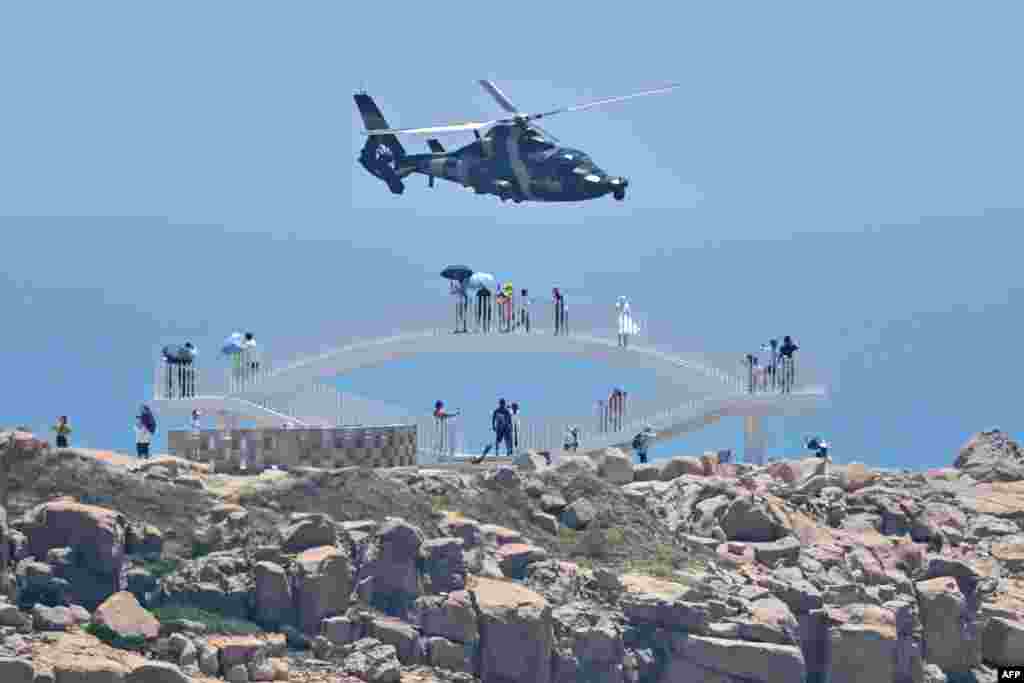 Tourists look on as a Chinese military helicopter flies past Pingtan island, one of mainland China's closest point from Taiwan, in Fujian province, ahead of massive military drills off Taiwan following U.S. House Speaker Nancy Pelosi's visit to the self-ruled island.