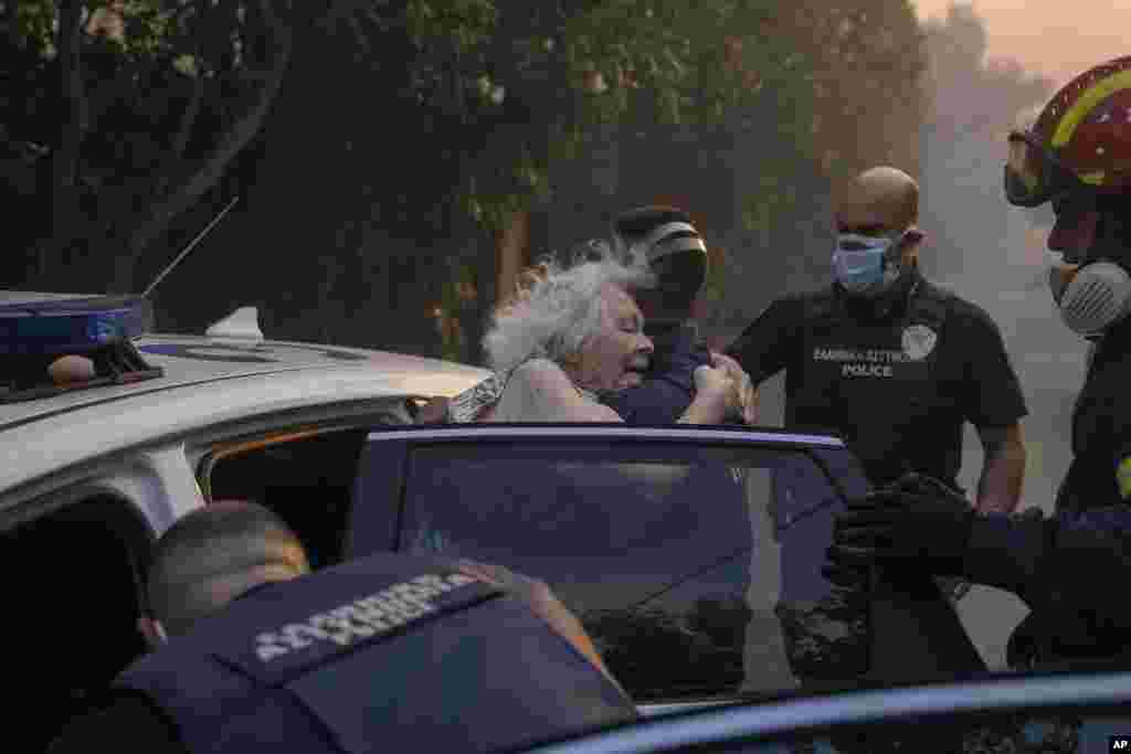 Firefighters and policemen evacuate an elderly woman from her house in Penteli, Greece. Hundreds of people were ordered to leave their homes after a large forest fire broke out northeast of Athens, fanned by high winds.