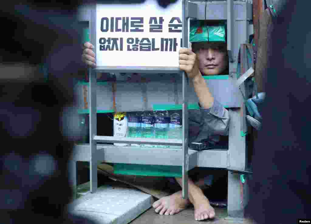 Yoo Choi-ahn, vice chief of the subcontractor union, attached inside a steel cage-like structure that he welded himself to on the floor of the occupied oil tanker, holds a sign during a strike at Daewoo Shipbuilding & Marine Engineering in Geoje, South Korea, July 19, 2022.