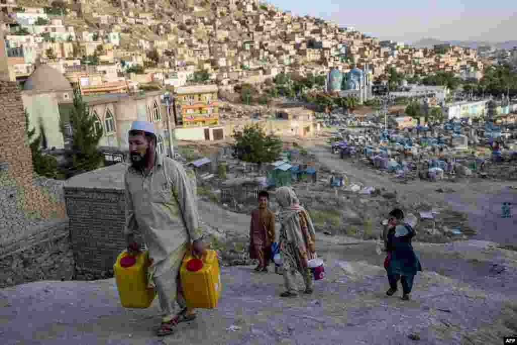 People carry drinking water in containers as they walk along a hillside near the Kart-e-Sakhi cemetery in Kabul, Afghanistan.