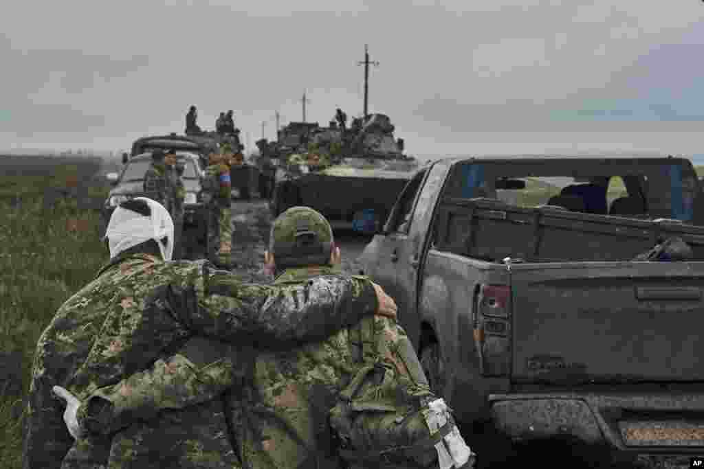 A Ukrainian soldier helps his wounded fellow soldier while military vehicles move on the road in the freed territory of the Kharkiv region, Sept. 12, 2022. Ukrainian troops retook a wide swath of territory from Russia, pushing Russian troops all the way back to the northeastern border in some places, and claiming to have captured many Russian soldiers.