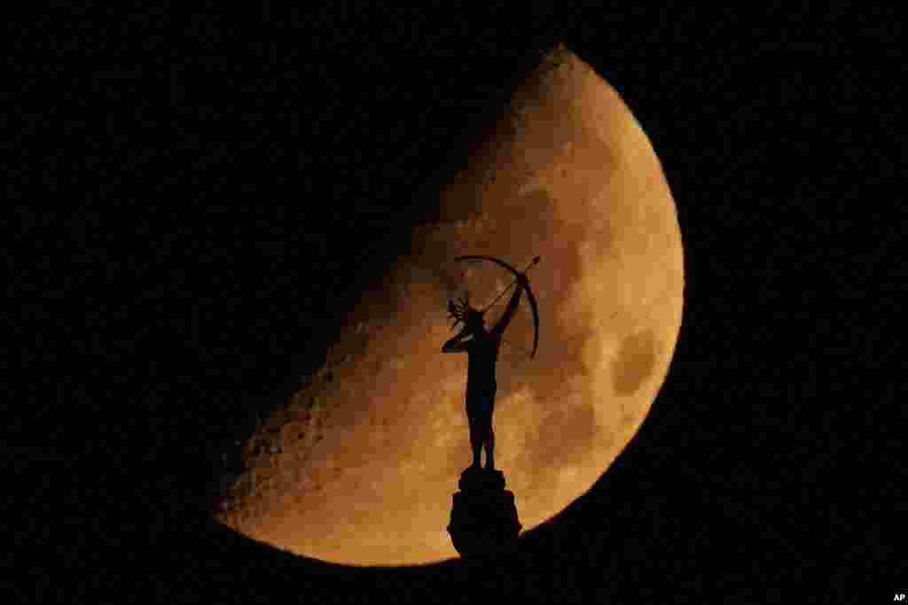 A statue of a Kansa warrior titled "Ad Astra," atop the Kansas Statehouse is silhouetted against the setting moon in Topeka, Kansas.