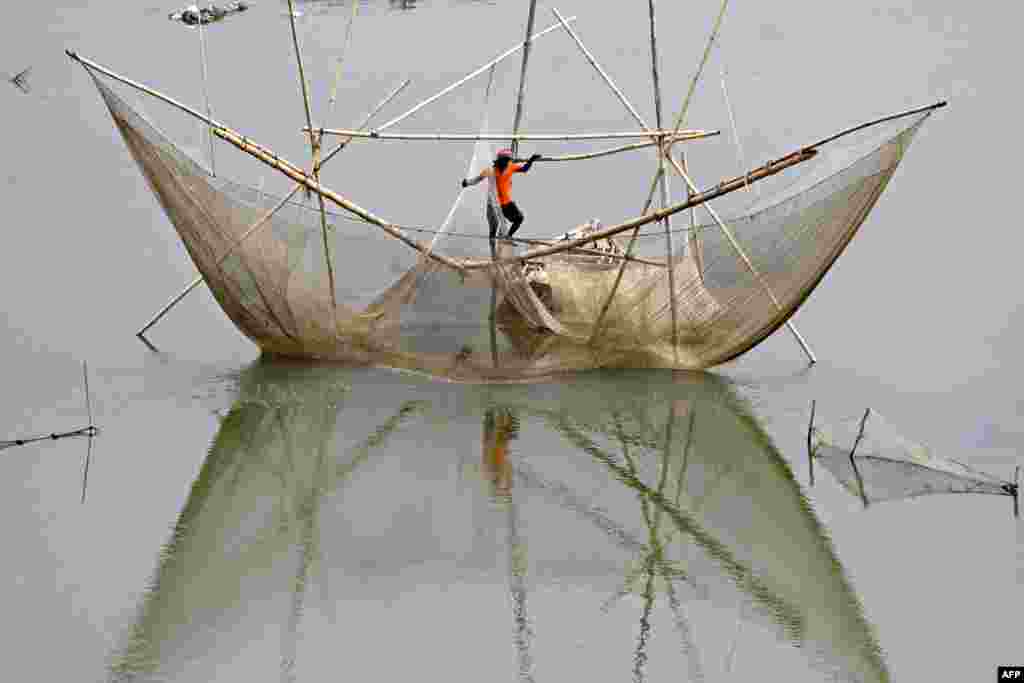 A fisherman stands on a fishing net in the waters of river Yamuna in New Delhi, India.