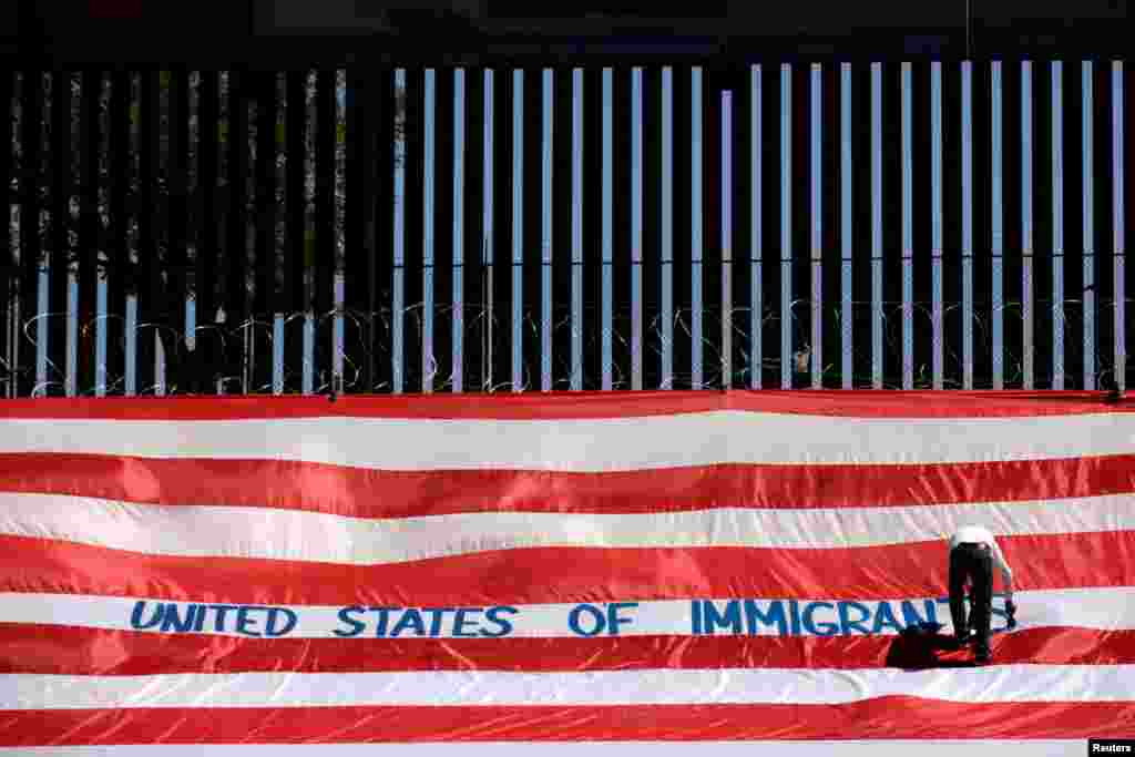 Roberto Marquez, known as Roberz, writes on a large U.S. flag as part of a protest called 'United States of Immigrants' to demand respect for migrants, near a border wall in El Paso, Texas, as pictured from Ciudad Juarez, Mexico, June 6, 2019.