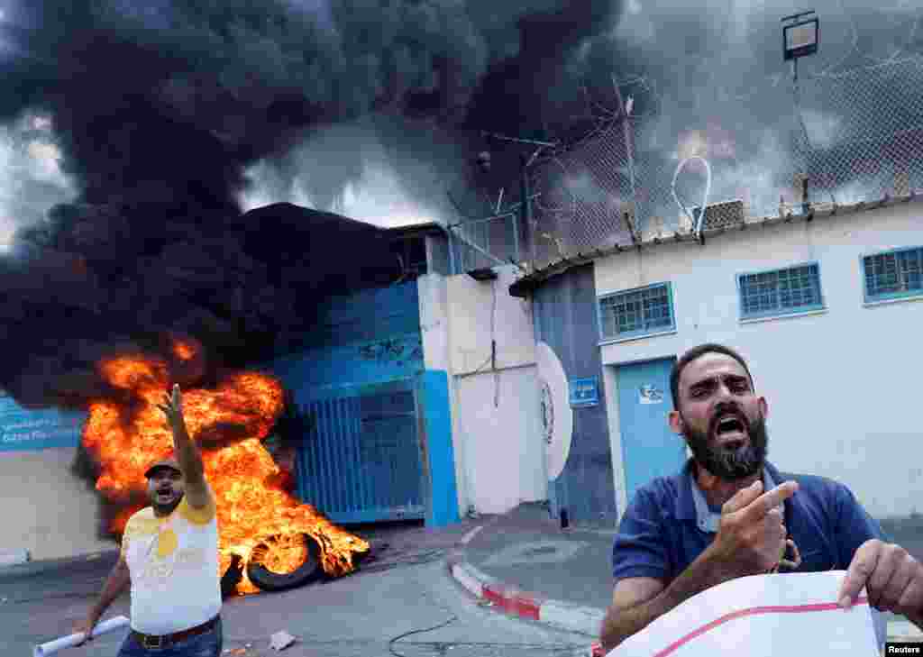Palestinian people burn tires outside the headquarters of the United Nations Works and Relief Agency (UNRWA) in Gaza City during a protest demanding the UNRWA to rebuild their houses that were destroyed during the Israel-Gaza fighting in 2014.