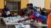 Funcionários da assembleia de voto organizam os boletins de voto antes de procederem à contagem numa assembleia de voto em Windhoek, Namíbia, em 1 de dezembro de 2024, durante a votação alargada após as eleições gerais do país. 