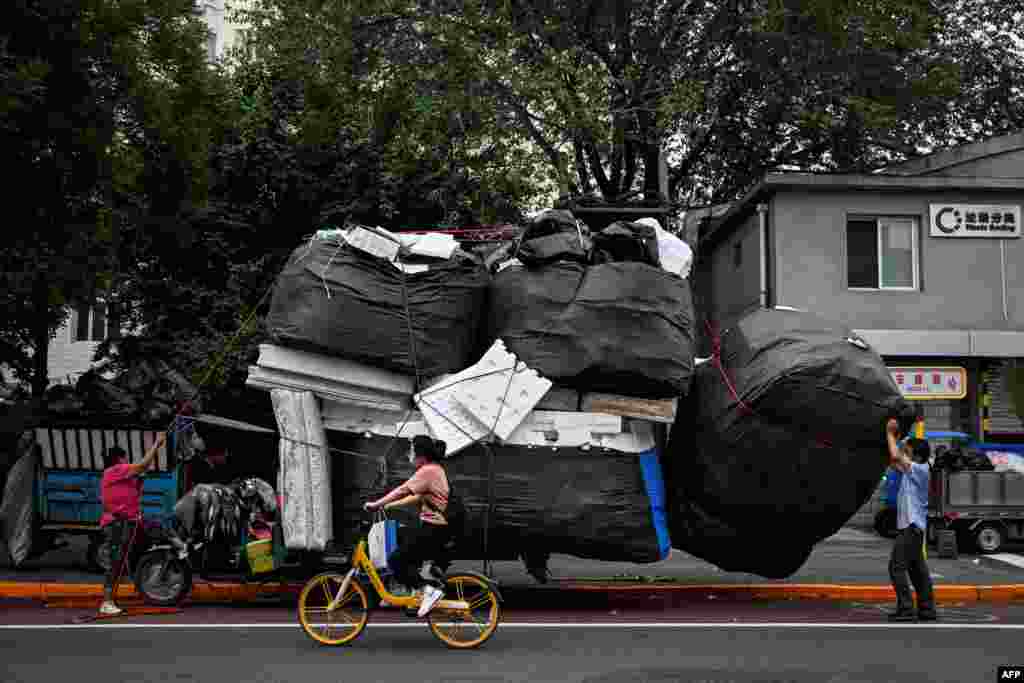 Workers load large sacks of foam and debris on a three-wheeled bike, in front of a waste sorting site in Beijing, China.