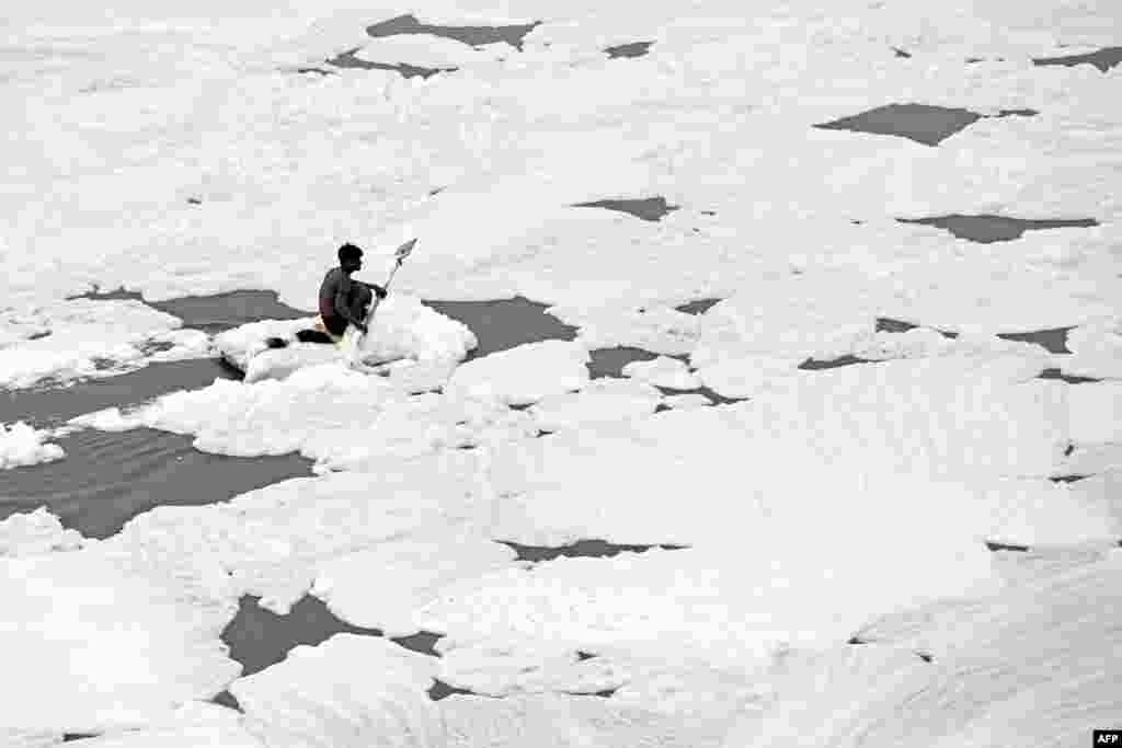 A man paddles his raft while collecting recyclable materials in the waters of river Yamuna, coated with polluted foam, in New Delhi, India.