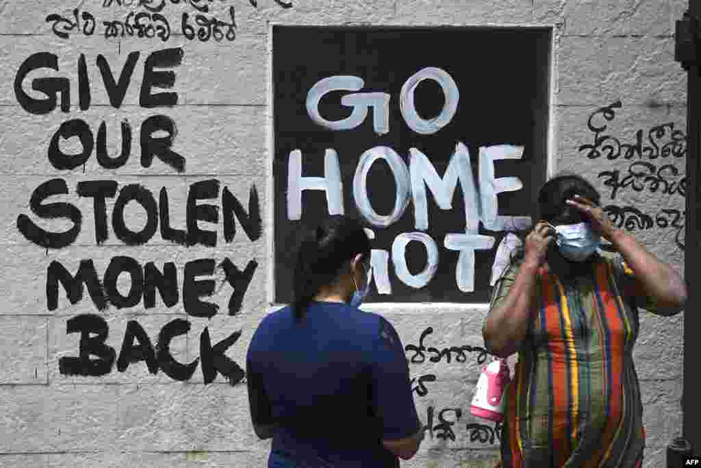 Women stand in front of a graffiti painted outside the premises of Sri Lanka's presidential palace, in Colombo, a day after it was overrun by anti-government protesters.