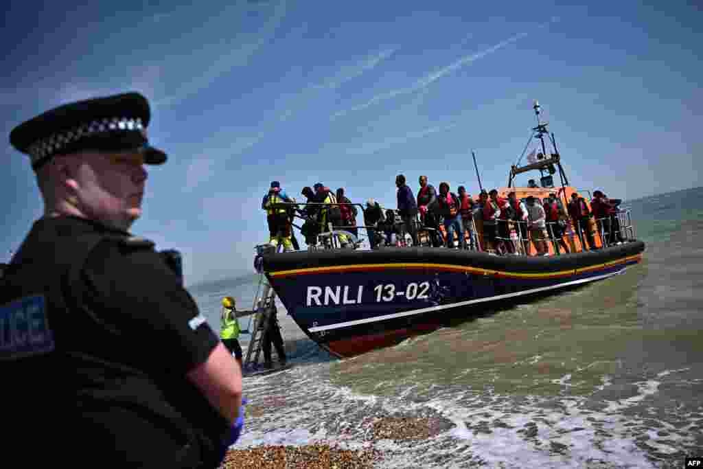 A British police officer stands guard on the beach of Dungeness, on the southeast coast of England, as Royal National Lifeboat Institution's staff members help migrants disembark from a lifeboat after they were picked up at sea while attempting to cross the English Channel. 