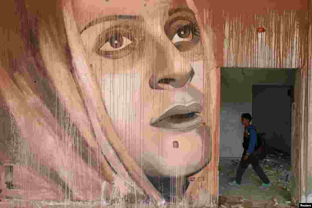 A schoolboy walks near a mural painted by Palestinian artist Ali al-Jabali in the remains of a building partially destroyed by Israeli air strikes, in Gaza City.