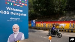 Un motociclista pasa junto a un graffiti en una pared que representa la lucha por la libertad de la India mientras se ve un cartel de bienvenida a los delegados a la izquierda, en Nueva Delhi, India, el 7 de septiembre de 2023.