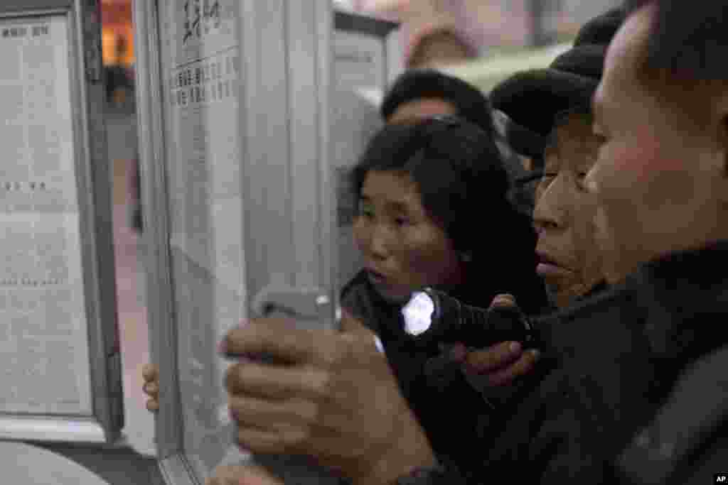 A North Korean man uses a flashlight as he and other subway commuters gather around a public newspaper stand on a train platform in Pyongyang to read headlines about Jang Song Thaek, North Korean leader Kim Jong Un's uncle, who was executed as a traitor.