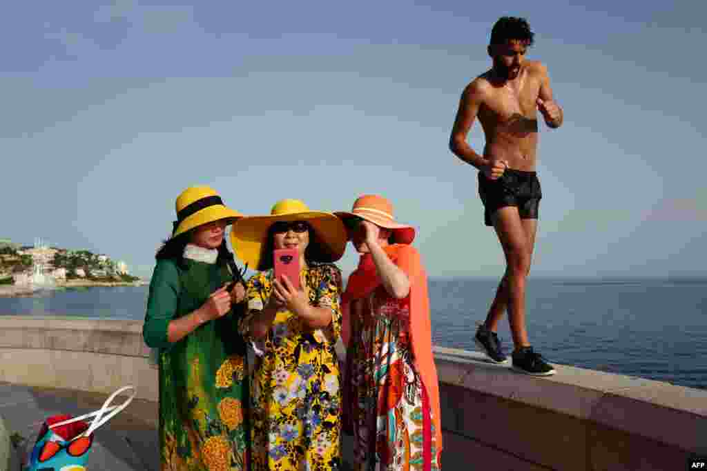 A man walks by as tourists take selfies on the French Riviera city of Nice, June 24, 2019, as temperatures soar to 33&deg;C (94&deg;F).