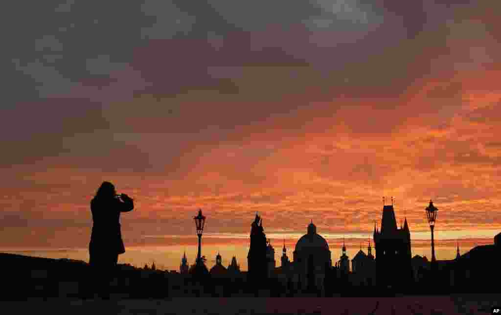 Woman takes a photograph of the medieval Charles Bridge as the sun rises in Prague, Czech Republic.